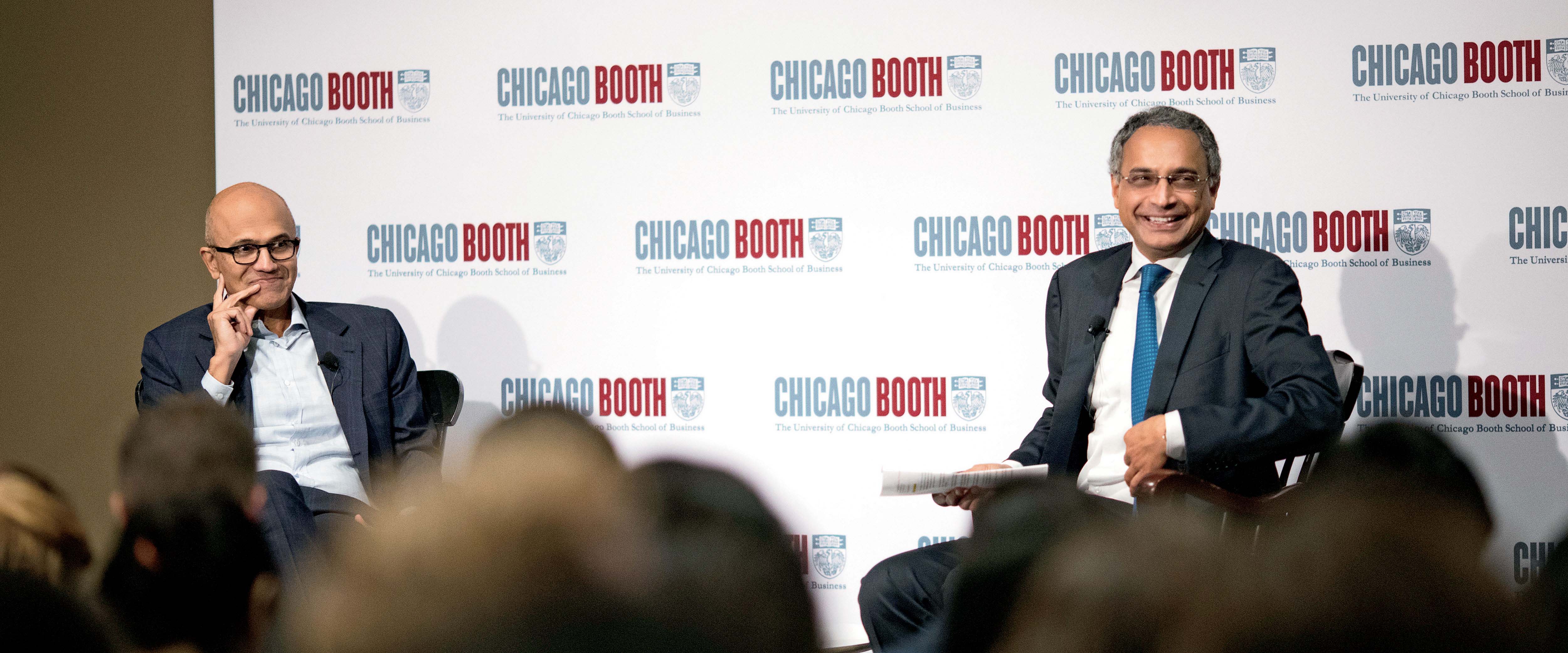Dean Madhav Rajan seated in front of a Chicago Booth sign with Microsoft Satya Nadella